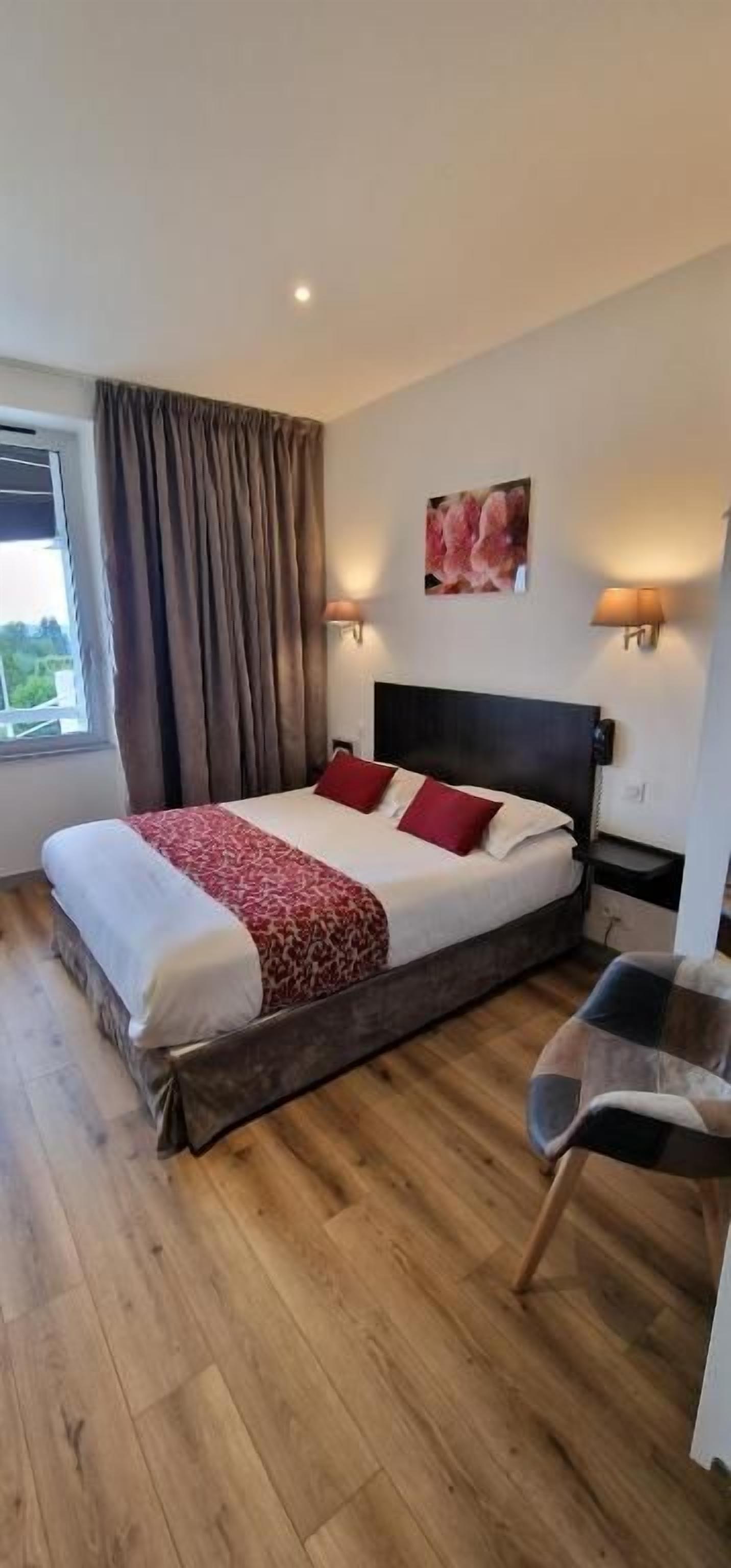 Une chambre d’hôtel avec un lit, une table de chevet, une lampe, une chaise et une fenêtre avec des rideaux.