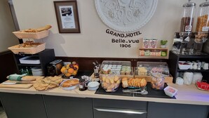A breakfast buffet with various breads, pastries, fruits, and condiments. - Hôtel Le Bellevue (Guer)