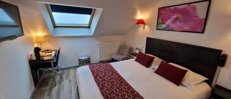 A bedroom with a bed, a desk, a chair, a radiator, a wall-mounted TV, and a skylight.