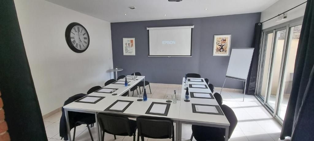 Una sala de conferencias con una larga mesa, sillas, una pantalla de proyector y una pizarra.