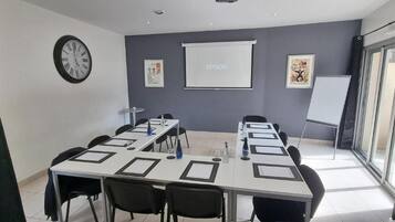 Una sala de conferencias con una larga mesa, sillas, una pantalla de proyector y una pizarra.
