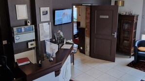 A reception area with a counter, a clock, a television, and a reception desk. - Hôtel Le Bellevue (Guer)