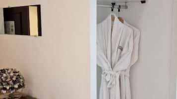 A room with a wooden dresser, a white robe hanging on a rack, and a shelf with pillows.
