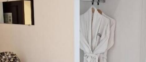 Una habitación con un aparador de madera, una bata blanca colgada en un perchero y una estantería con almohadas.