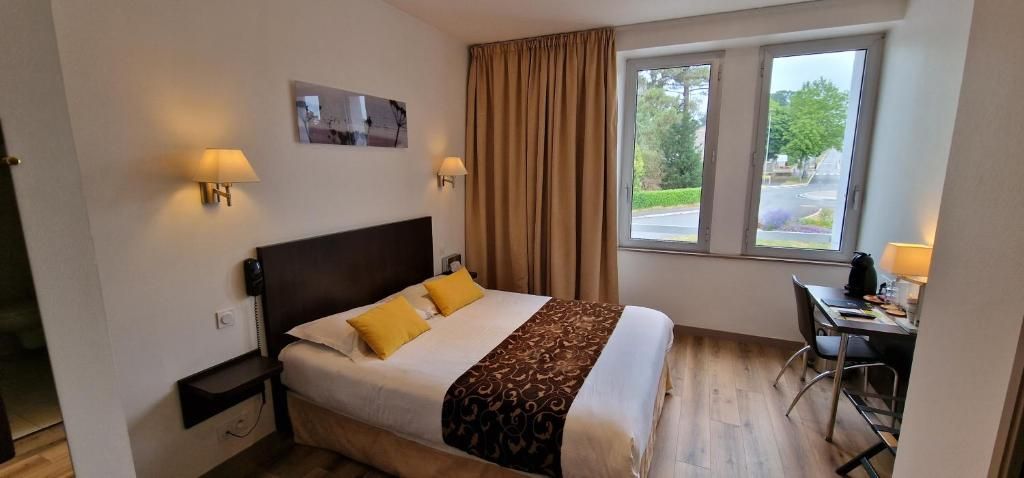 Une chambre d’hôtel avec un lit, des tables de chevet, un bureau et une fenêtre avec des rideaux.