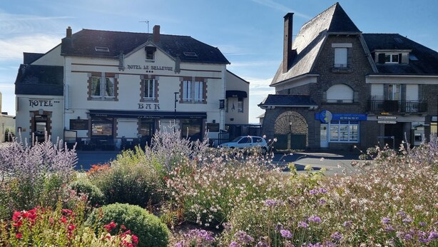 A hotel with a bar, surrounded by colorful flowers and a street. - Hôtel Le Bellevue (Guer)