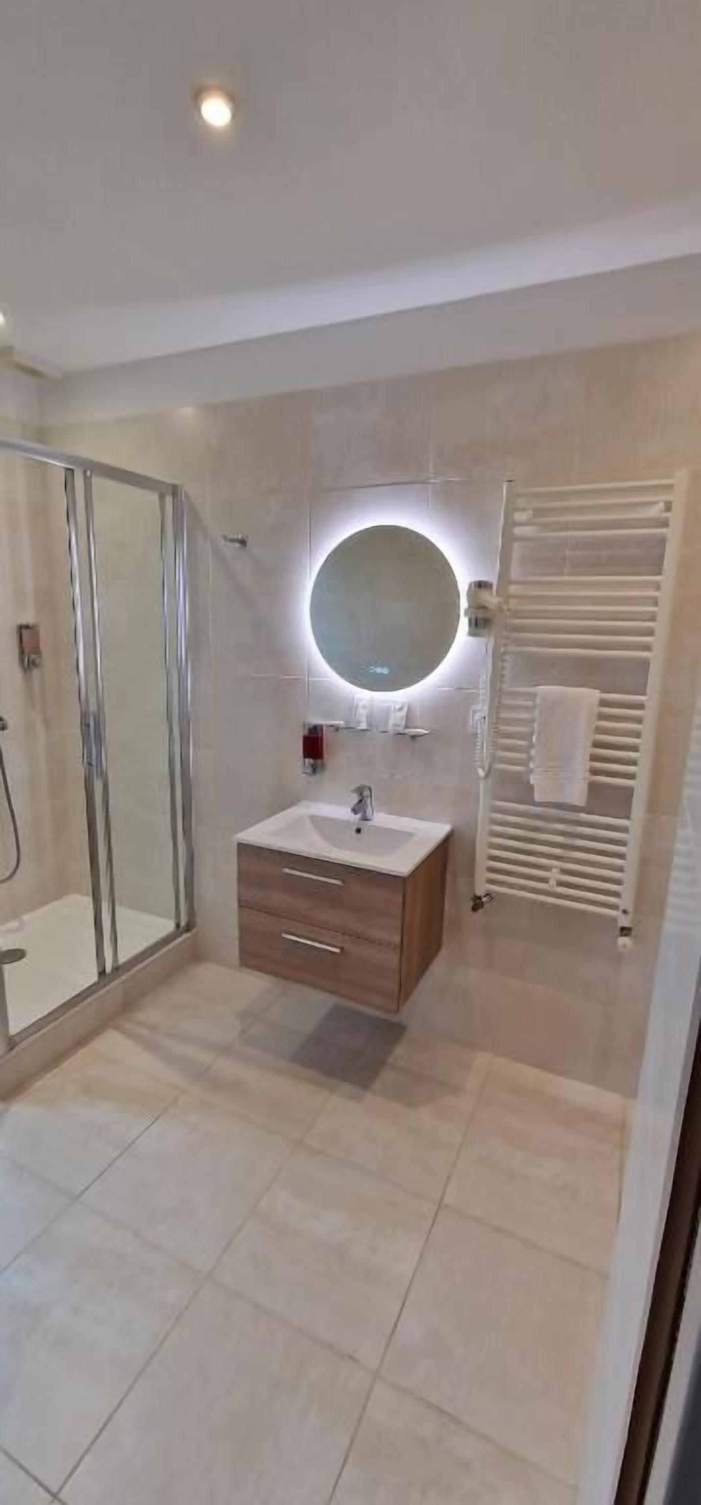 Een moderne badkamer met een douchecabine van glas, een houten wastafelmeubel en een spiegel bevestigd aan de muur.