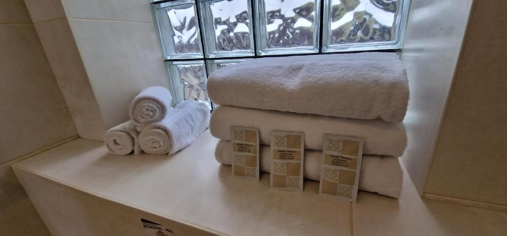 A bathroom with a window, a towel rack with rolled towels, and a stack of towels on a counter.