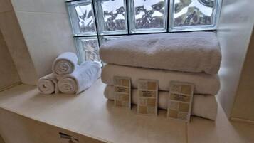A bathroom with a window, a towel rack with rolled towels, and a stack of towels on a counter.