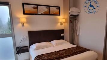 A hotel room with a bed, two wall-mounted lamps, a window, and a wheelchair accessibility sign.