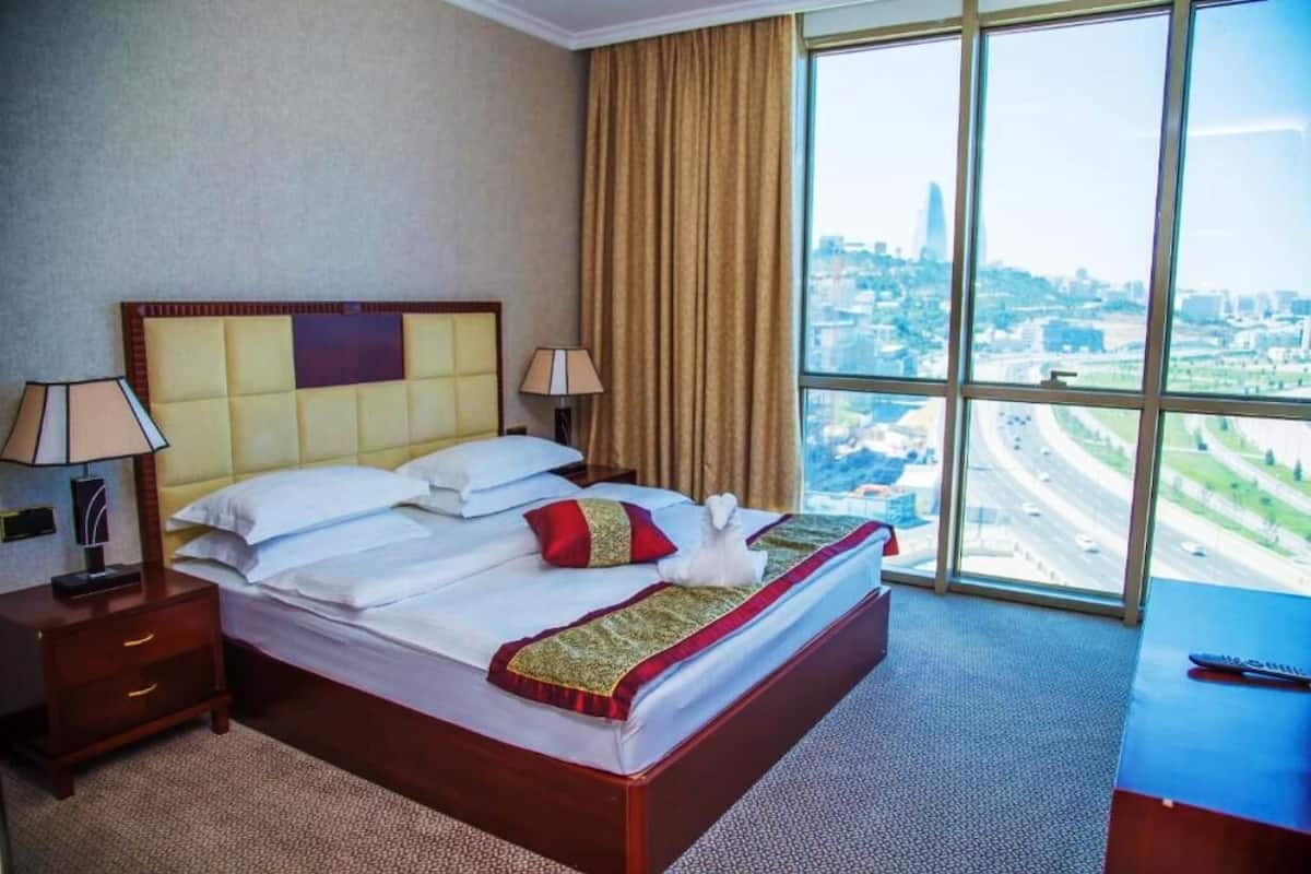 Une chambre d’hôtel avec un grand lit, deux tables de chevet, une vue sur le paysage urbain à travers de grandes fenêtres et une rue de la ville visible à l’extérieur.
