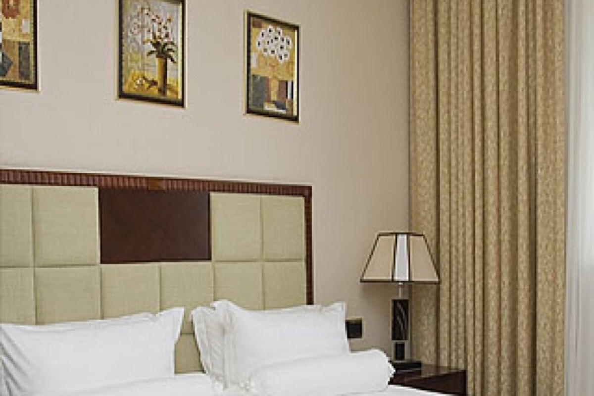 Een hotelkamer met een groot bed, hoofdeinde, nachtkastje, lamp en drie ingelijste foto's aan de wand.