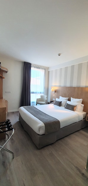 Habitación de hotel con una cama grande, un escritorio, una silla y un ventanal con cortinas.