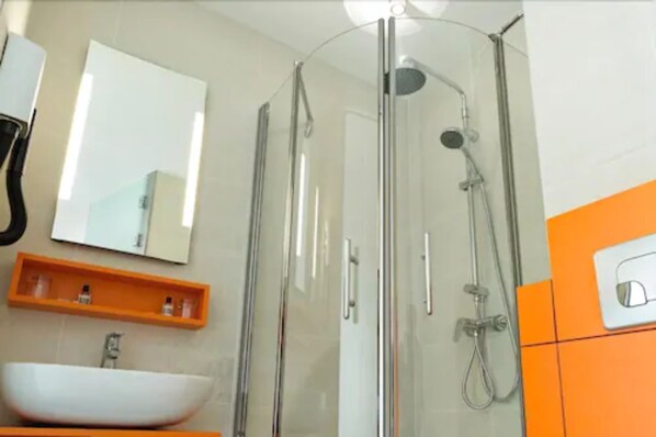 Un baño moderno con ducha envuelta en vidrio, un lavabo blanco y estantes de almacenamiento naranja.