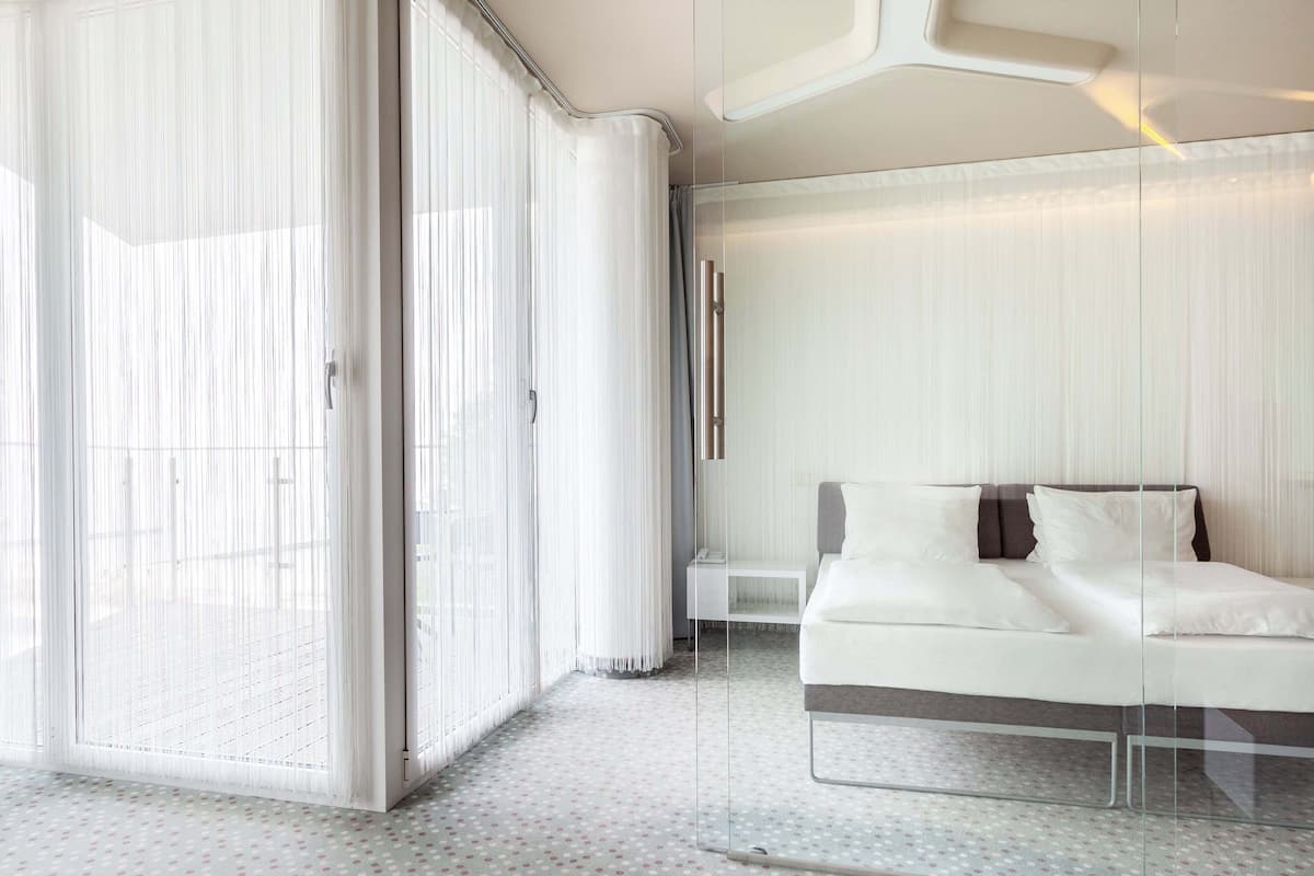 Una habitación de hotel moderna con un separador de vidrio, una cama con ropa de cama blanca y un suelo estampado.