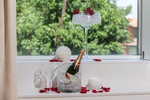 A window with a view of greenery, a champagne bottle in a glass, and a martini glass with strawberries. - A. Montesinho (Braganca)