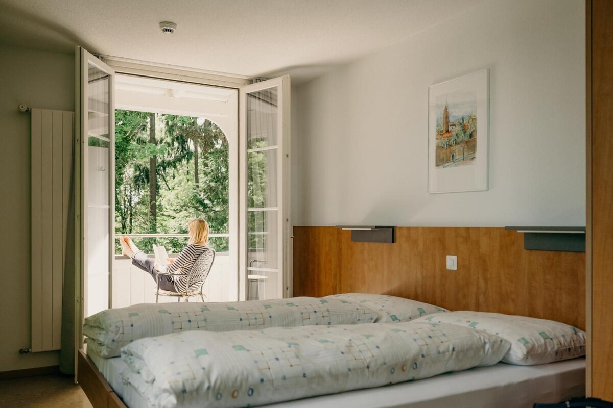 A bedroom with a large bed, a window with a view of trees, and a chair by the window.