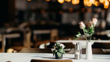 A restaurant interior with a table set for dining, featuring a vase with flowers and a candle.