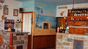 Uma área de bar com bancada de pedra, prateleiras de madeira com garrafas e um mural na parede.