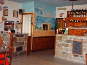 Un área de bar con una barra de piedra, estantes de madera con botellas y un mural en la pared.