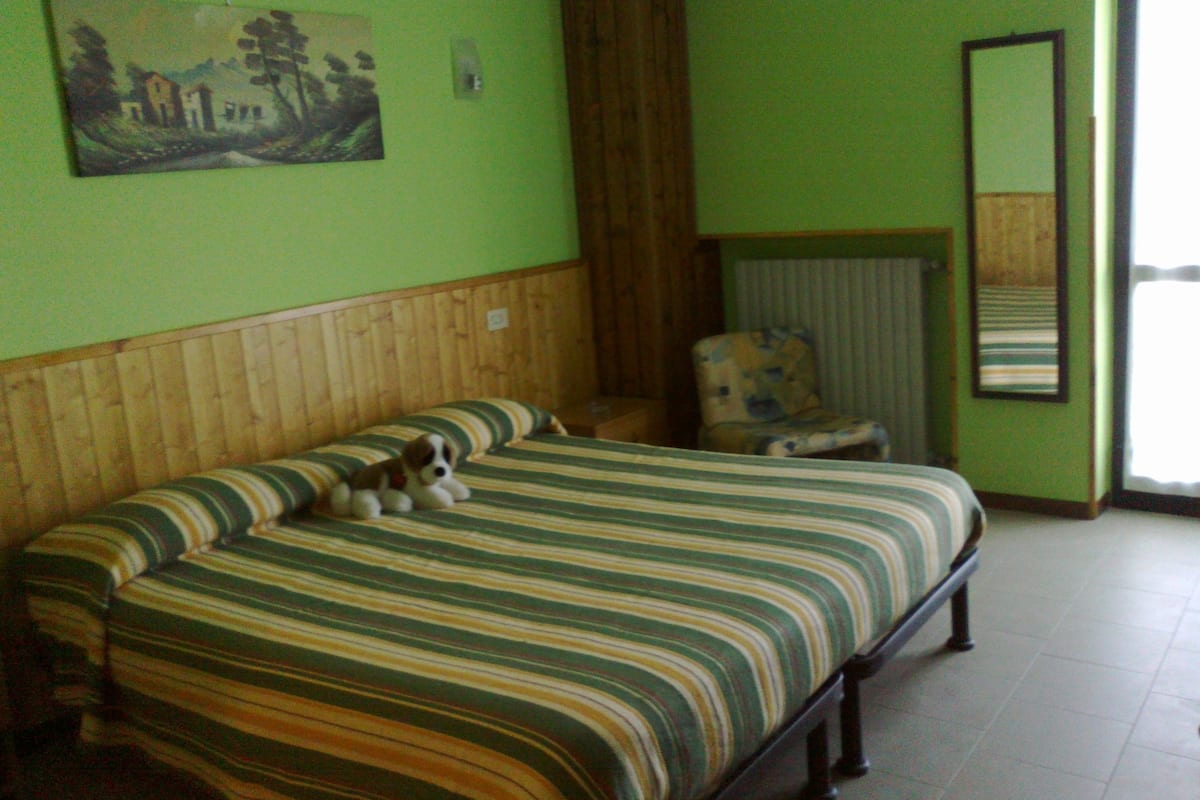 Una habitación con cama, una silla, un cuadro en la pared y una ventana.