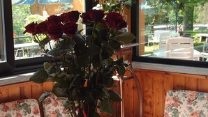 Uma mesa com um vaso de rosas vermelhas em um vaso de vidro transparente, paredes com painéis de madeira e cadeiras estofadas com padrão floral.