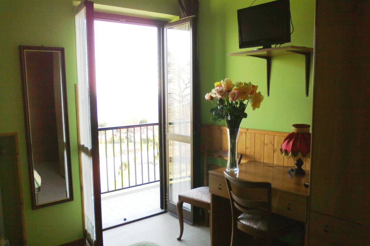 Una habitación con cama, un escritorio con silla, un televisor en la pared y una ventana con vistas al exterior.