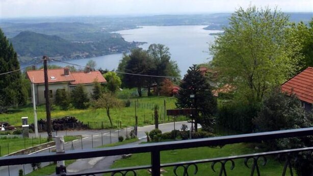 Uma varanda com vista para um lago, uma estrada e casas ao fundo.