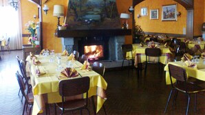 Um restaurante com mesas postas para refeições, lareira e obras de arte nas paredes.