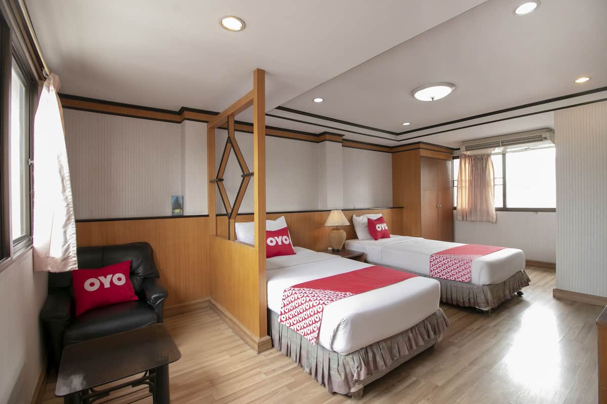 A hotel room with two beds, a wooden chair, a small table, and a window with curtains.