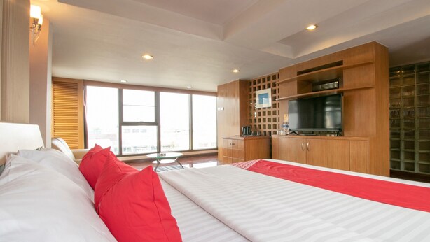 A hotel room with a bed, a TV, wooden cabinets, and a window with a city view. - Hotel Win Long (Bangkok)