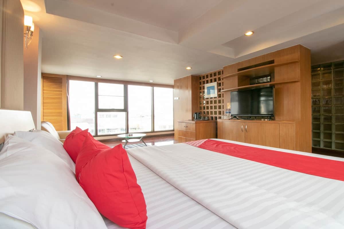 A hotel room with a bed, a TV, wooden cabinets, and a window with a city view.
