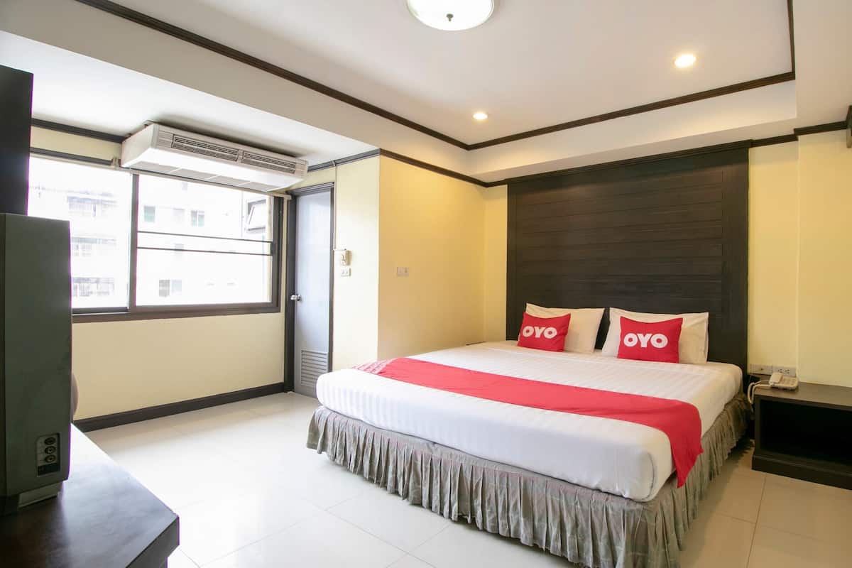 A hotel room with a large bed, a bedside table, a desk, and a window with an air conditioning unit.
