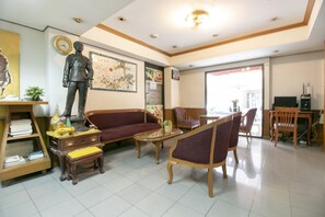 A living room with a sofa, armchairs, a coffee table, and a statue. There is a bookshelf and a dining area with chairs and a table. - Hotel Win Long (Bangkok)