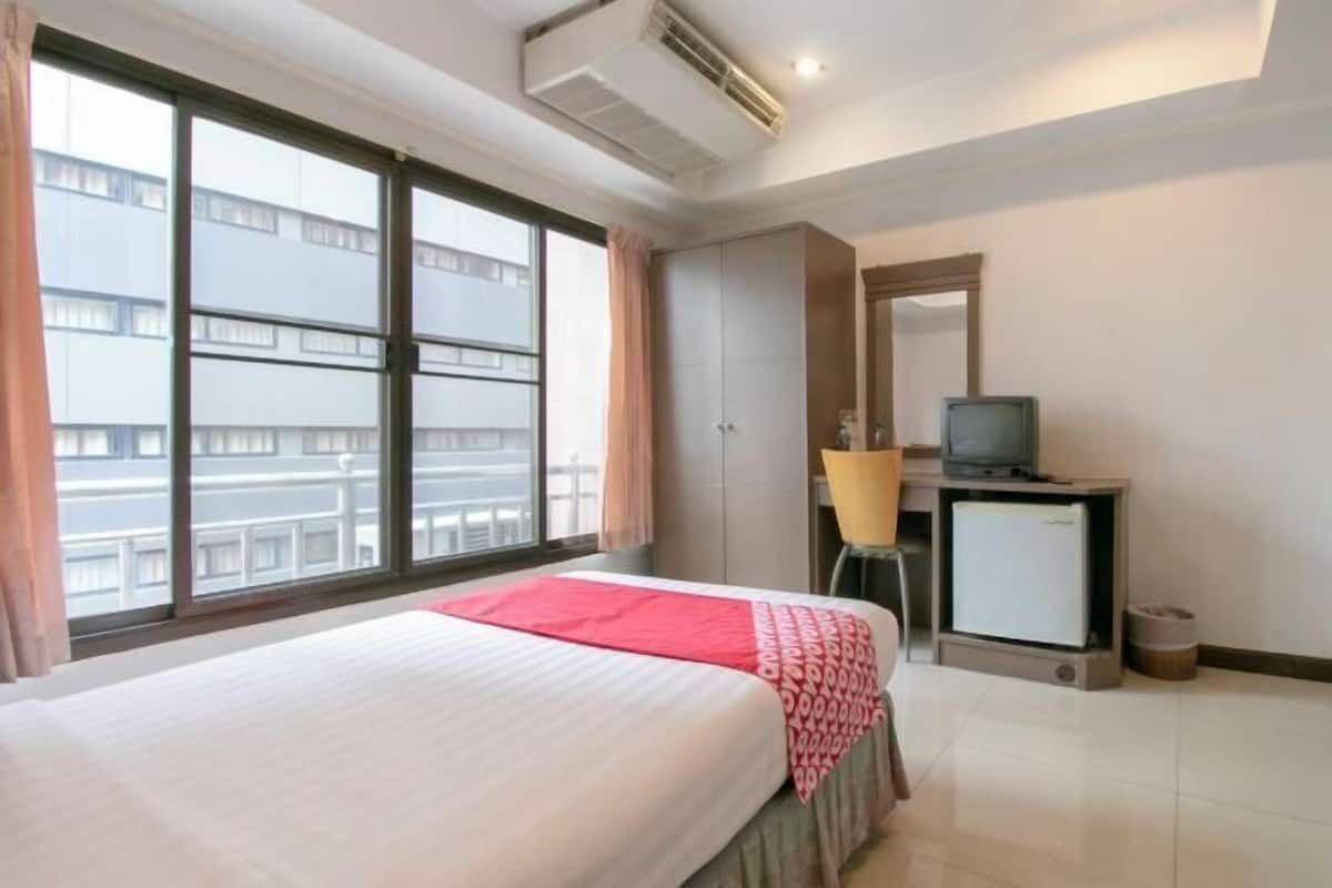 A hotel room with a bed, a TV, a small desk, and a window with a view of buildings.