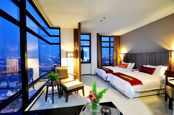 A modern hotel room with a large city view, a bed, a sofa, and a small table with a vase of flowers. - Grand Howard Hotel Bangkok (Bangkok)