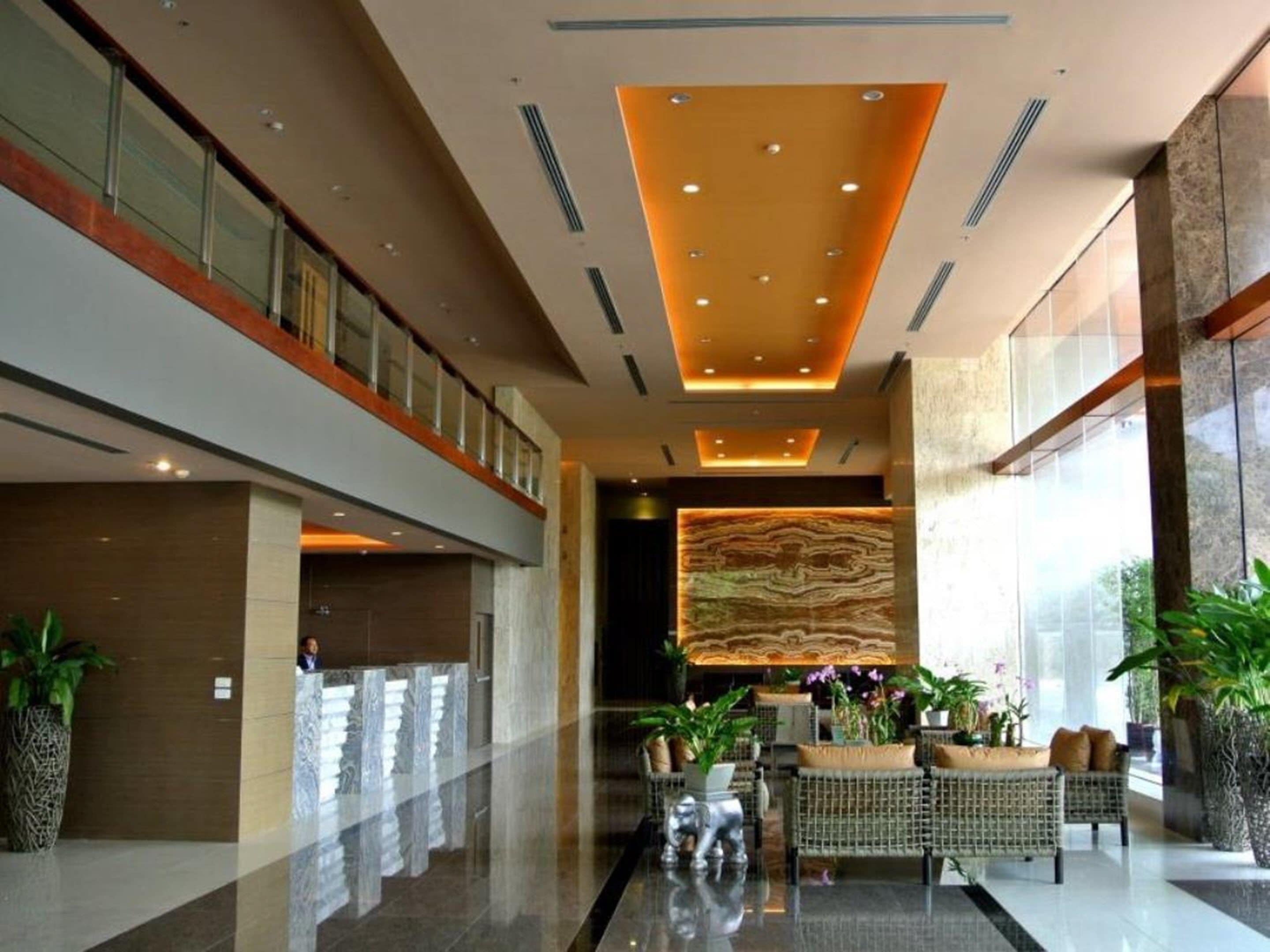 A spacious lobby with a high ceiling, a reception desk, and seating areas with plants.