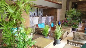 Un vestíbulo con muebles de mimbre, plantas en macetas y una recepción.