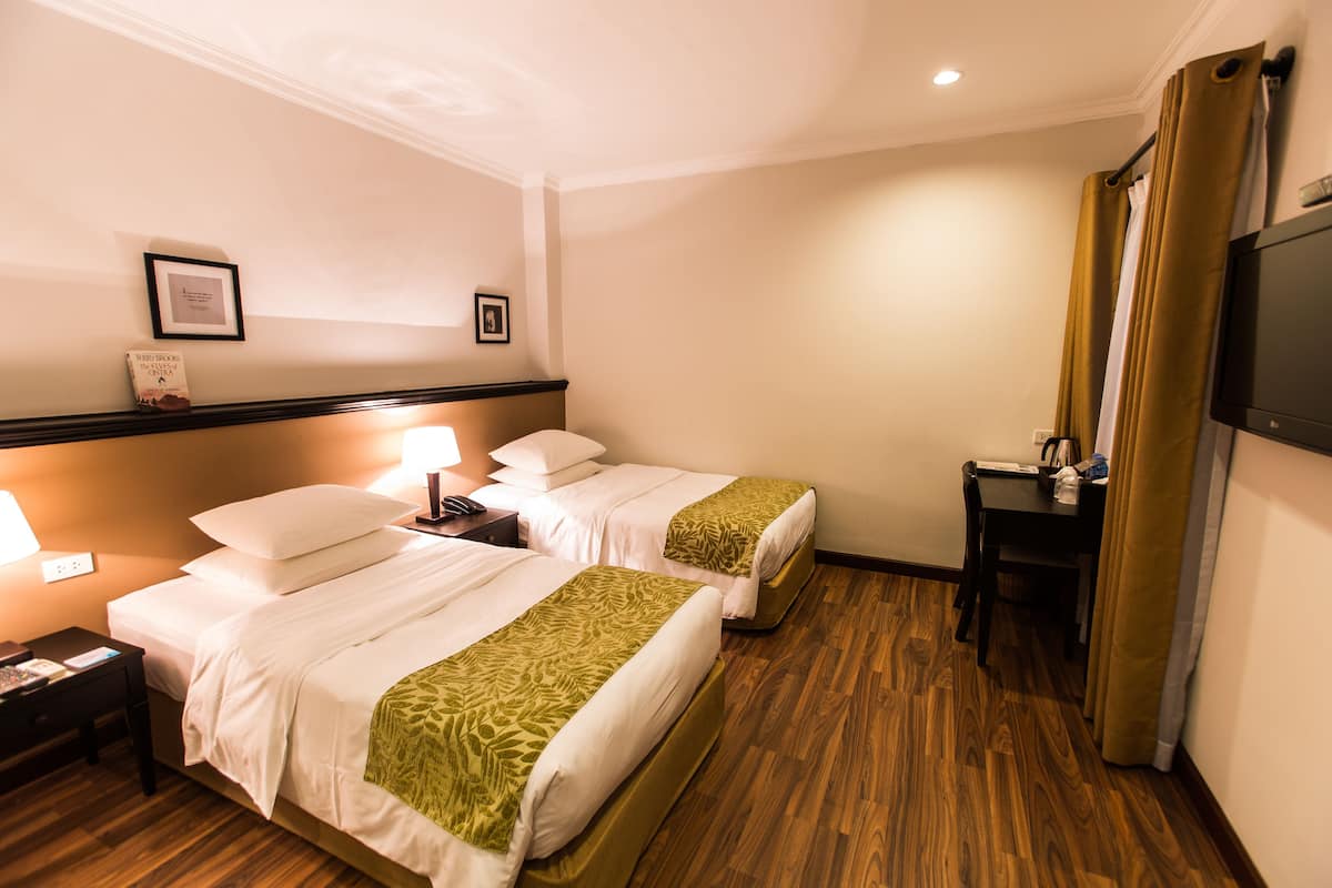 A hotel room with two beds, a desk, a TV, and a nightstand with a lamp.