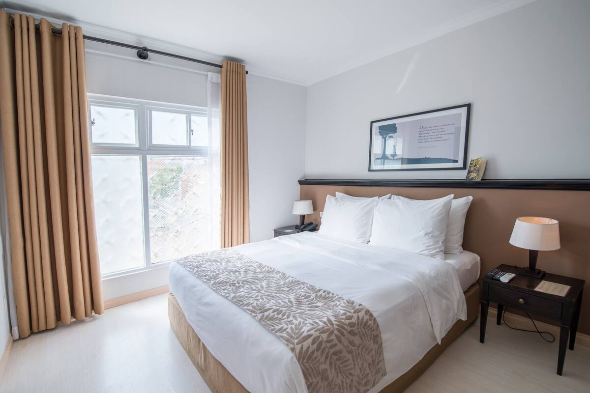 A hotel room with a large bed, two bedside tables with lamps, a framed picture on the wall, and a window with curtains.