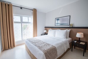 A hotel room with a large bed, two bedside tables with lamps, a framed picture on the wall, and a window with curtains. - The Alcove Library Hotel (Ho Chi Minh City)
