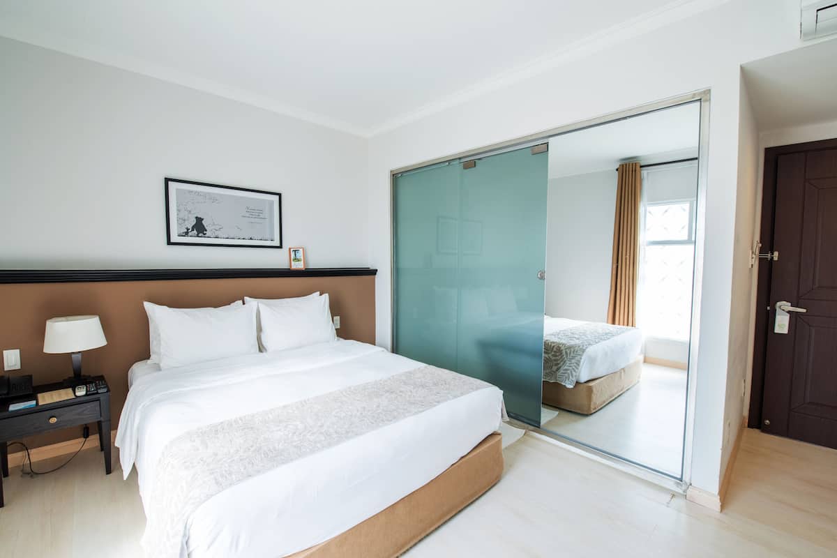 A hotel room with a large bed, a bedside table with a lamp, a framed picture on the wall, and a sliding glass door leading to another room.