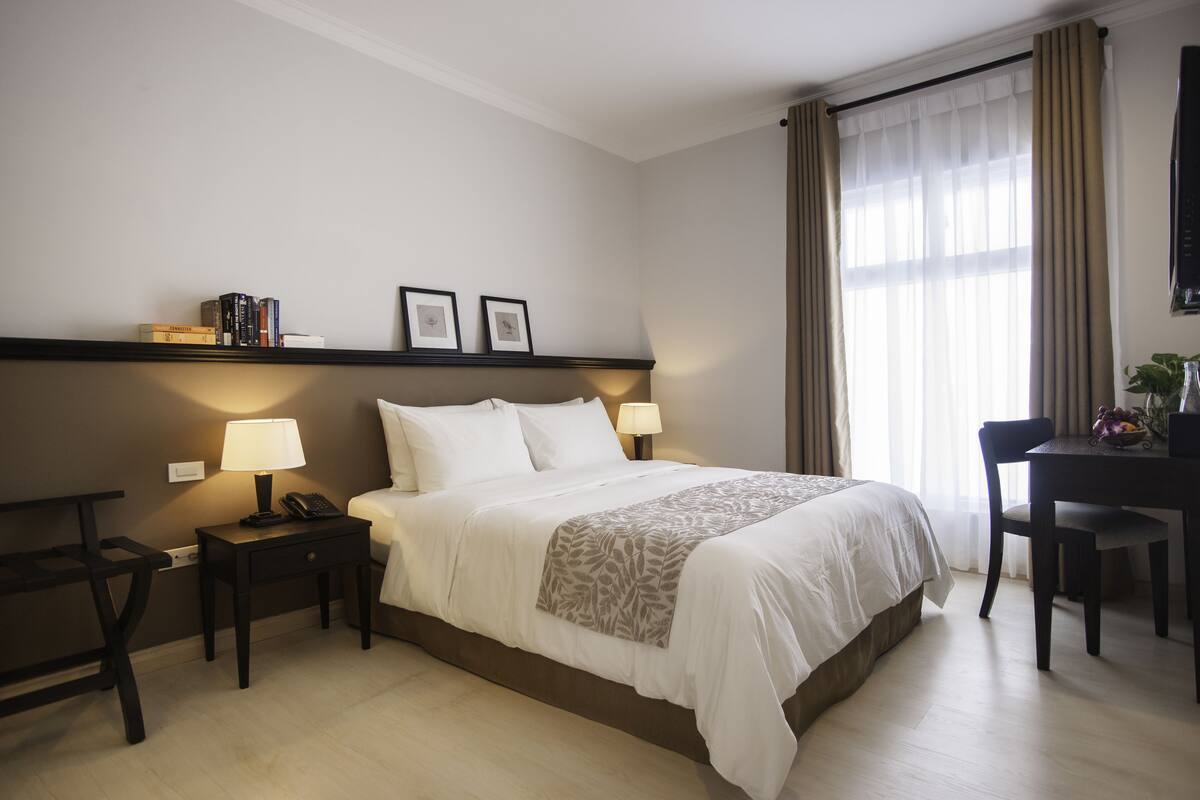 A hotel room with a bed, bedside tables, lamps, a desk, and a chair.