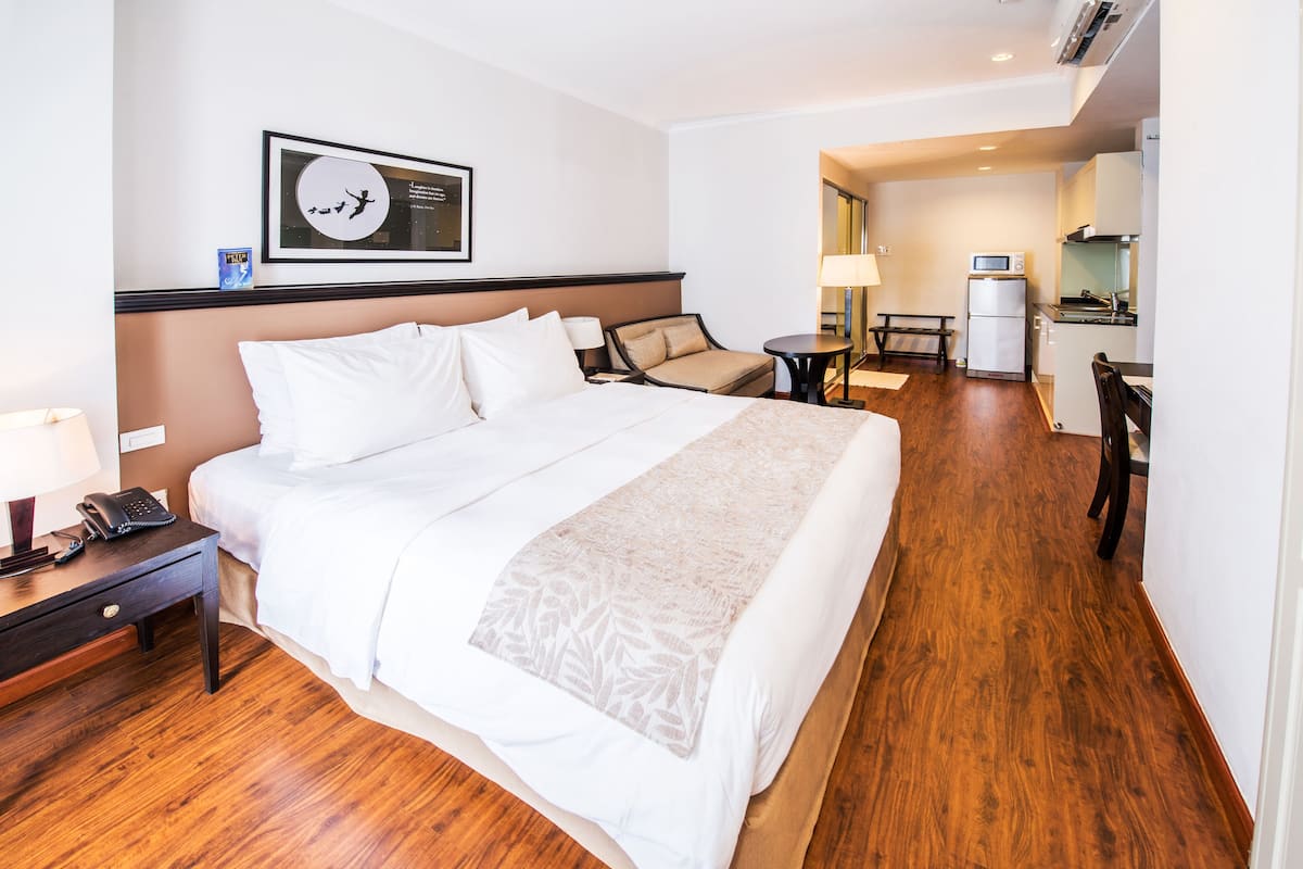 A hotel room with a large bed, a desk with a phone, a chair, a small table, a microwave, and a refrigerator in the kitchenette.