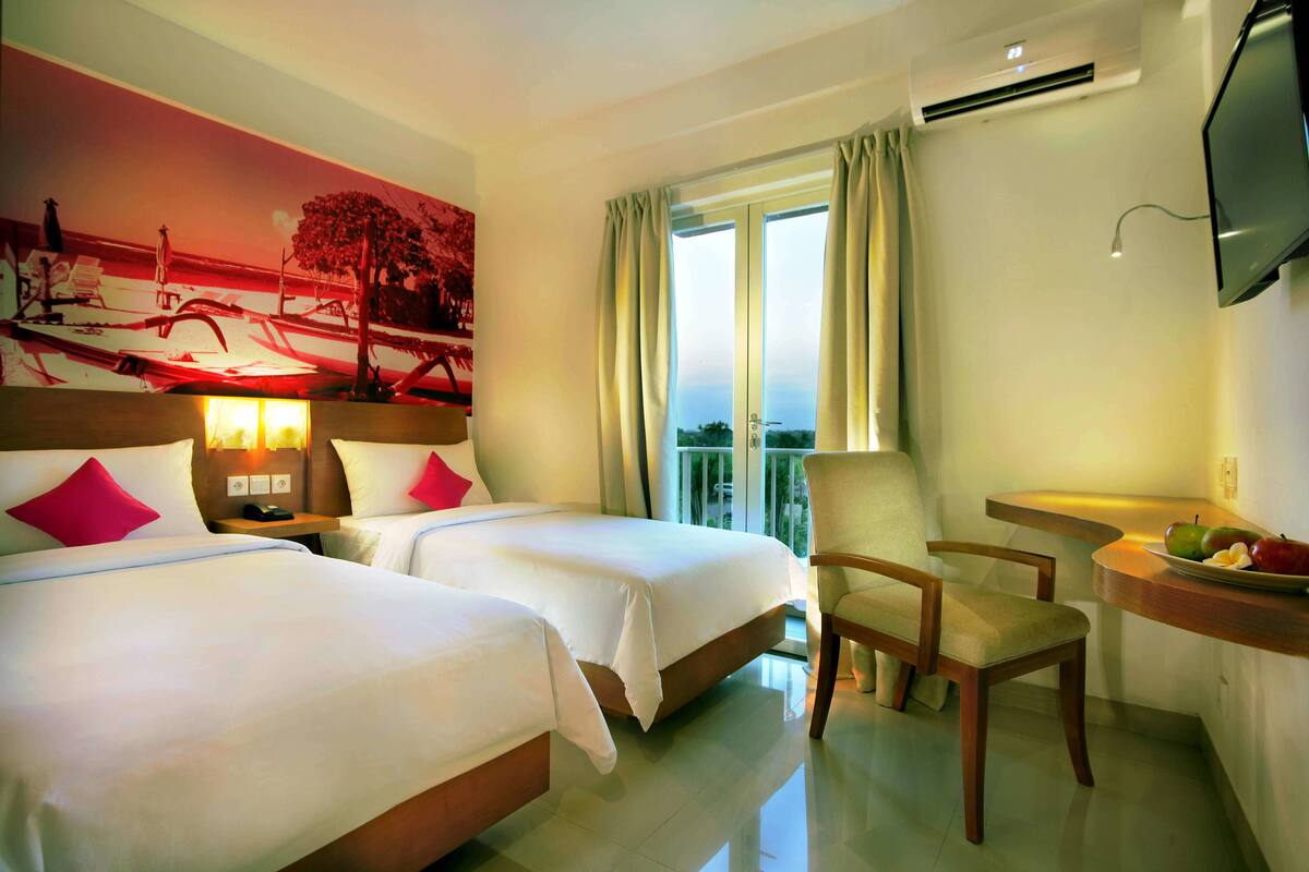 A hotel room with two beds, a desk with a chair, a TV, and a window with curtains.