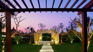 A covered outdoor area with a tiled pathway leading to a central entrance, surrounded by greenery and palm trees. - Seminyak Garden (Seminyak)