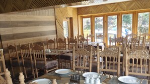 A dining area with a large wooden table set for six, surrounded by intricately carved chairs. - Hotel Noor Mahal (Anantnag)