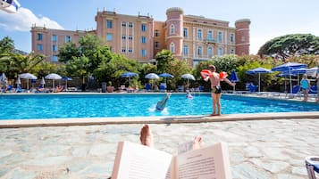Relax by the pool surrounded by lounge chairs and umbrellas, with a tower in the background.