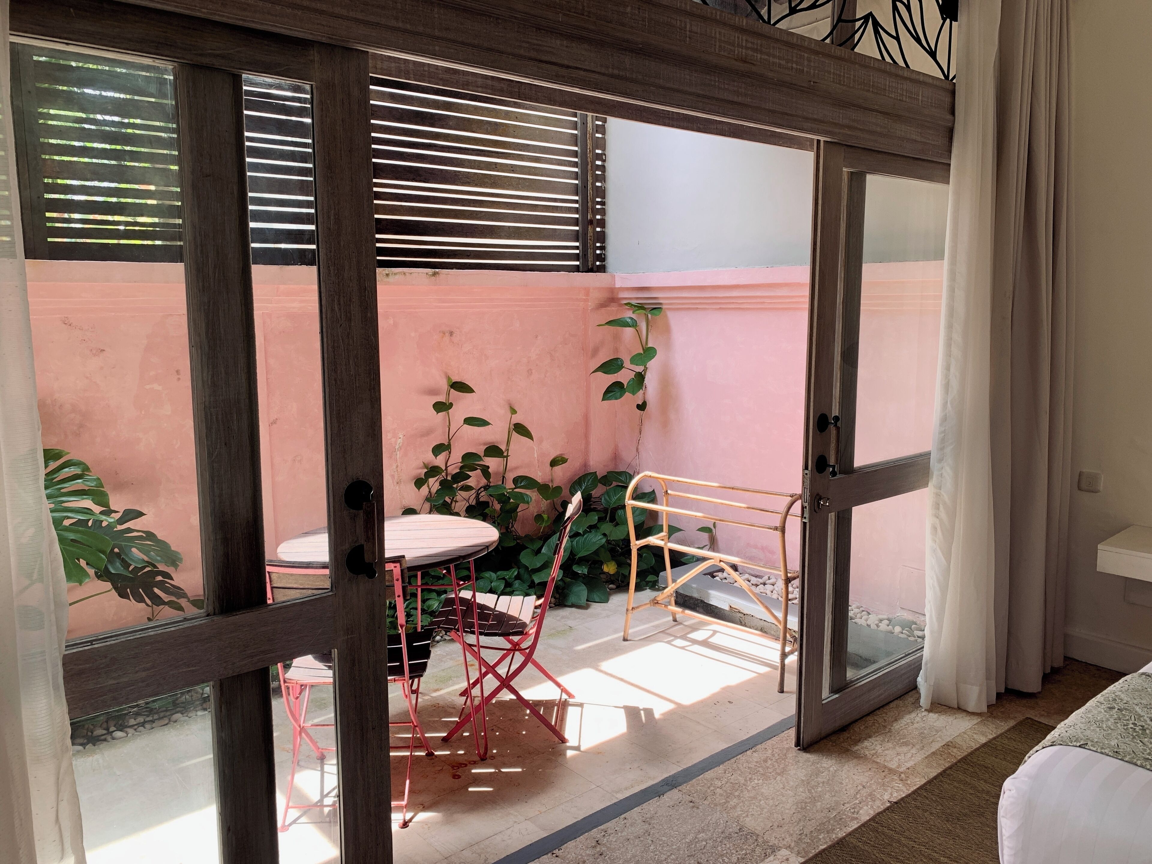 Una stanza con una porta scorrevole in vetro che dà su uno spazio esterno con tavolo e sedie, un piccolo giardino e vista sulla strada.