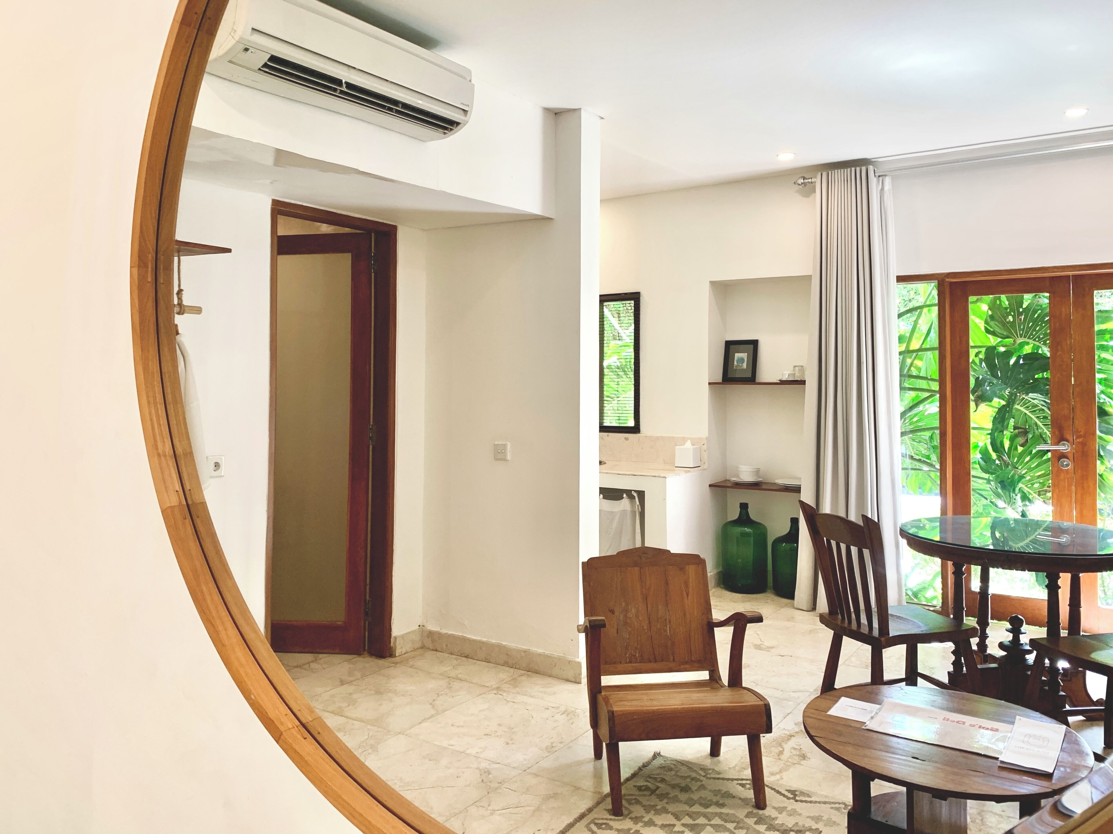 A room with a wooden door, a round table with chairs, a small rug, and a window with curtains.